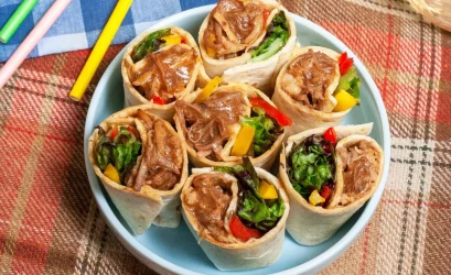 A blue bowl atop a picnic blanket. The bowl is filled with pulled pork tortilla wraps.